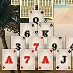 Cartas de un juego de solitario dispuestas en una estructura piramidal frente a un fondo con palmeras y montañas