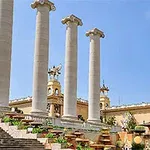 Columnas altas y blancas frente a una estructura con decoración clásica y cielo azul de fondo