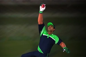 Un jugador de críquet atrapa una pelota en el aire, usando un uniforme azul con detalles verdes y una gorra a juego