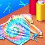 Camiseta con diseño tie-dye colorido sobre una mesa de madera, acompañada de botellas de tinte de colores rojo, amarillo y azul, con fondo azul decorado con íconos de tijeras y aguja