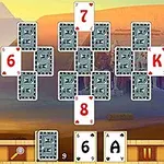 Cartas de juego de solitario dispuestas en un patrón sobre un fondo temático del Antiguo Egipto, con estatuas y un paisaje desértico