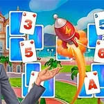 Una mujer sonriente con cabello rubio sostiene un objeto mientras un cohete rojo se eleva entre cartas de juego numeradas, en un entorno colorido