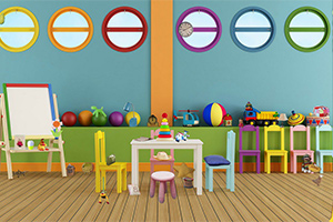 Aula de juegos colorida con mesas, sillas, juguetes y una pizarra en una habitación con paredes de círculos coloridos