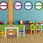 Aula de juegos colorida con mesas, sillas, juguetes y una pizarra en una habitación con paredes de círculos coloridos