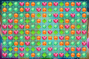 Tablero colorido con gemas en forma de corazones rosas, diamantes verdes, y hexágonos naranjas dispuestas en una cuadrícula