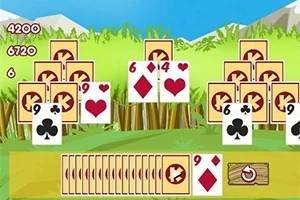 Cartas de juego dispersas sobre un fondo de pasto verde con montañas al fondo y una fila de cartas boca abajo al frente