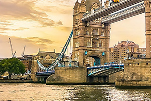 Puente de piedra y acero con torres en un río al atardecer