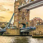 Puente de piedra y acero con torres en un río al atardecer