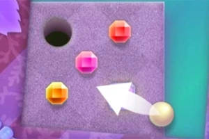 Un tablero con fondo morado que tiene un hoyo negro, tres gemas de colores naranja, rosa y amarillo, y una flecha blanca señalando una esfera amarilla