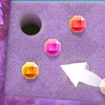 Un tablero con fondo morado que tiene un hoyo negro, tres gemas de colores naranja, rosa y amarillo, y una flecha blanca señalando una esfera amarilla