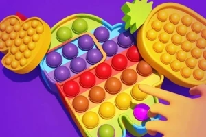 Juguete de burbujas de colores en forma de personaje entre frutas sobre un fondo morado, con una mano interactuando