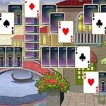 Cartas de juego dispuestas en un patrón piramidal sobre un fondo de canal con puente y edificaciones