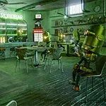 Interior de una cafetería futurista con robots sentados en mesas y un letrero luminoso en la barra