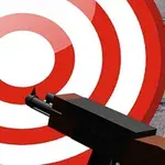 Un objetivo de tiro rojo y blanco con un arma apuntando hacia él frente a una pared de ladrillos