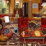 Una sala con decoración oriental llena de objetos dispersos, incluyendo alfombras elaboradas, sillas rojas y jarrones