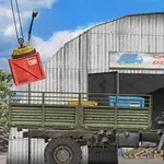 Camión de carga estacionado frente a un almacén con un contenedor rojo suspendido por una grúa