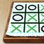 Tablero de papel cuadriculado con un juego de tres en línea usando círculos negros y equis verdes sobre una superficie de madera
