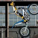Motociclista realizando acrobacias en una motocicleta frente a un fondo industrial