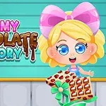 Niña con moño rosa sosteniendo una bandeja de chocolates decorados frente a un fondo turquesa con el texto Yummy Chocolate Factory
