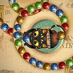 Una figura de animal negro con ojos amarillos y dientes blancos en un entorno con esferas de colores sobre un fondo con motivos egipcios